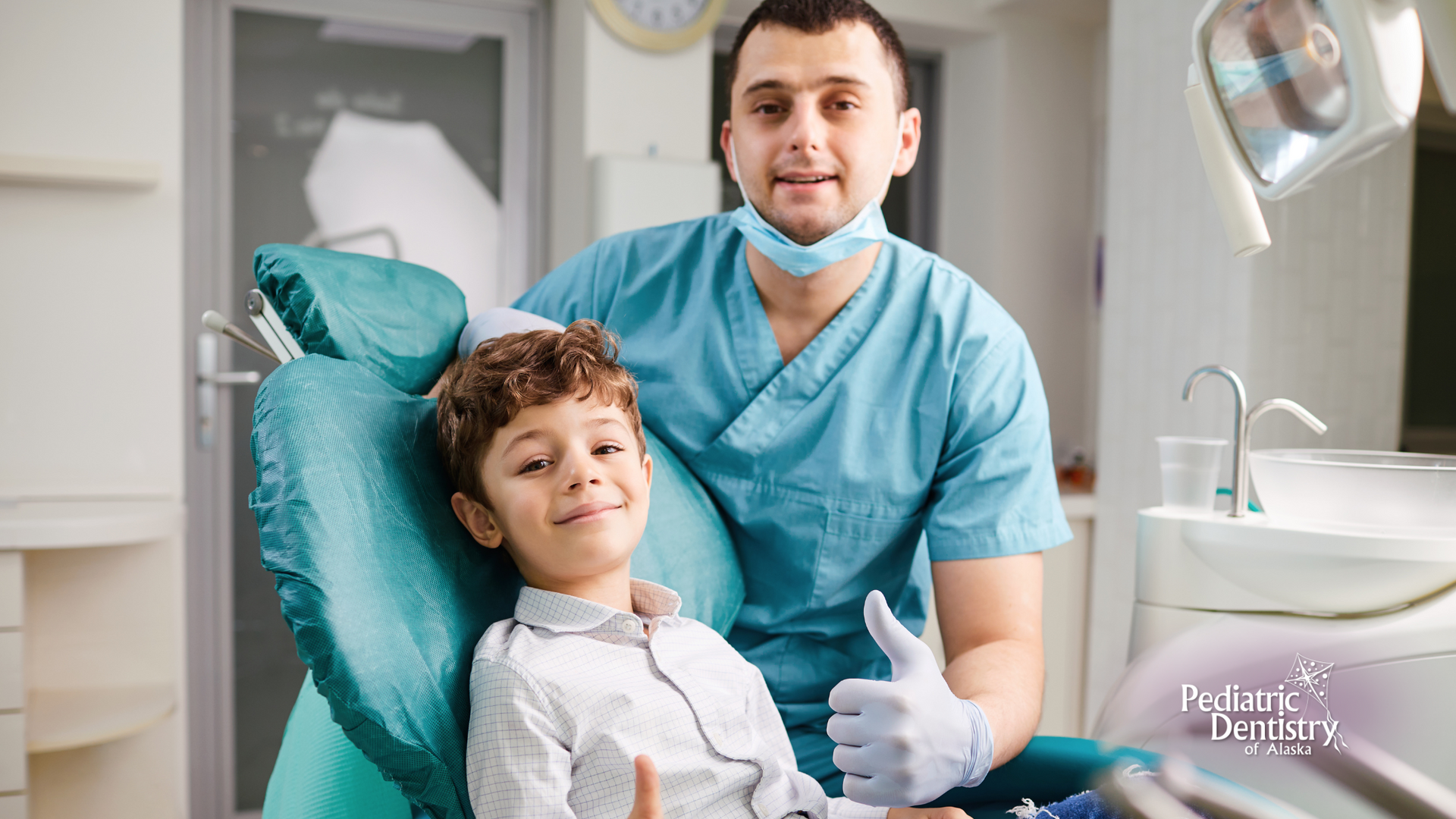 A young boy is sitting in a dental chair and giving a thumbs up.