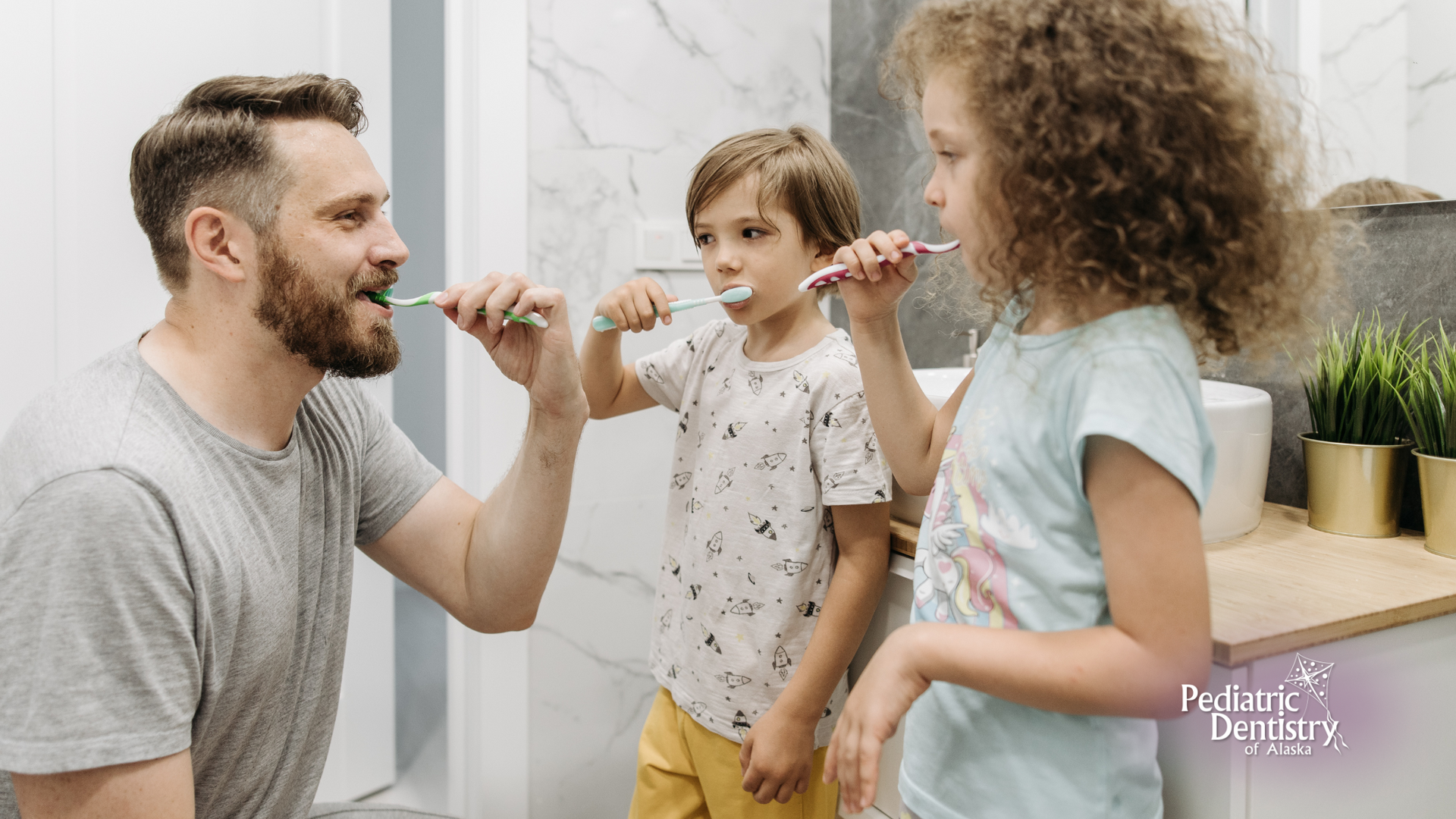 A man and two children are brushing their teeth in a bathroom.