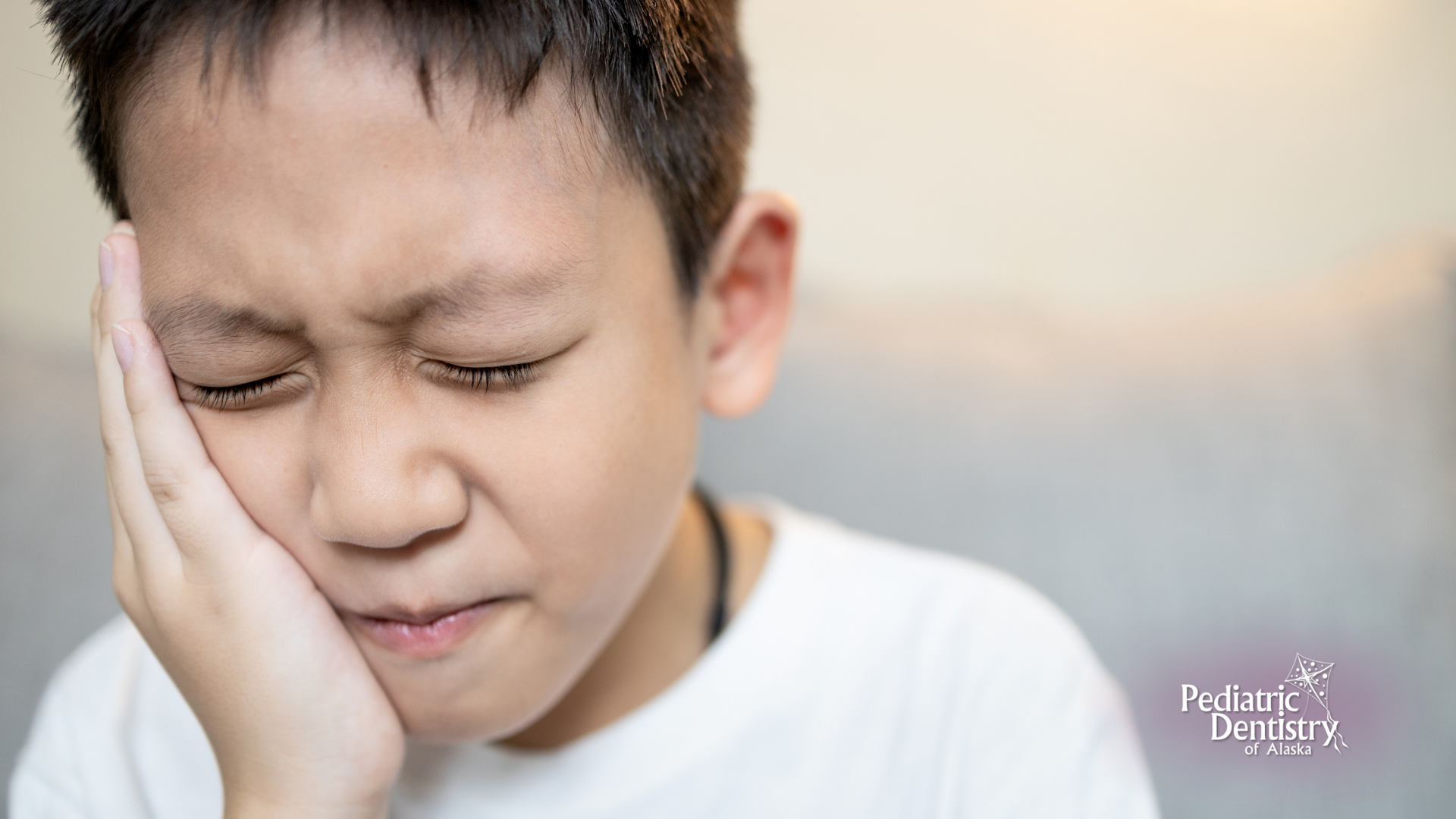 A young boy is holding his face in pain because of a toothache.