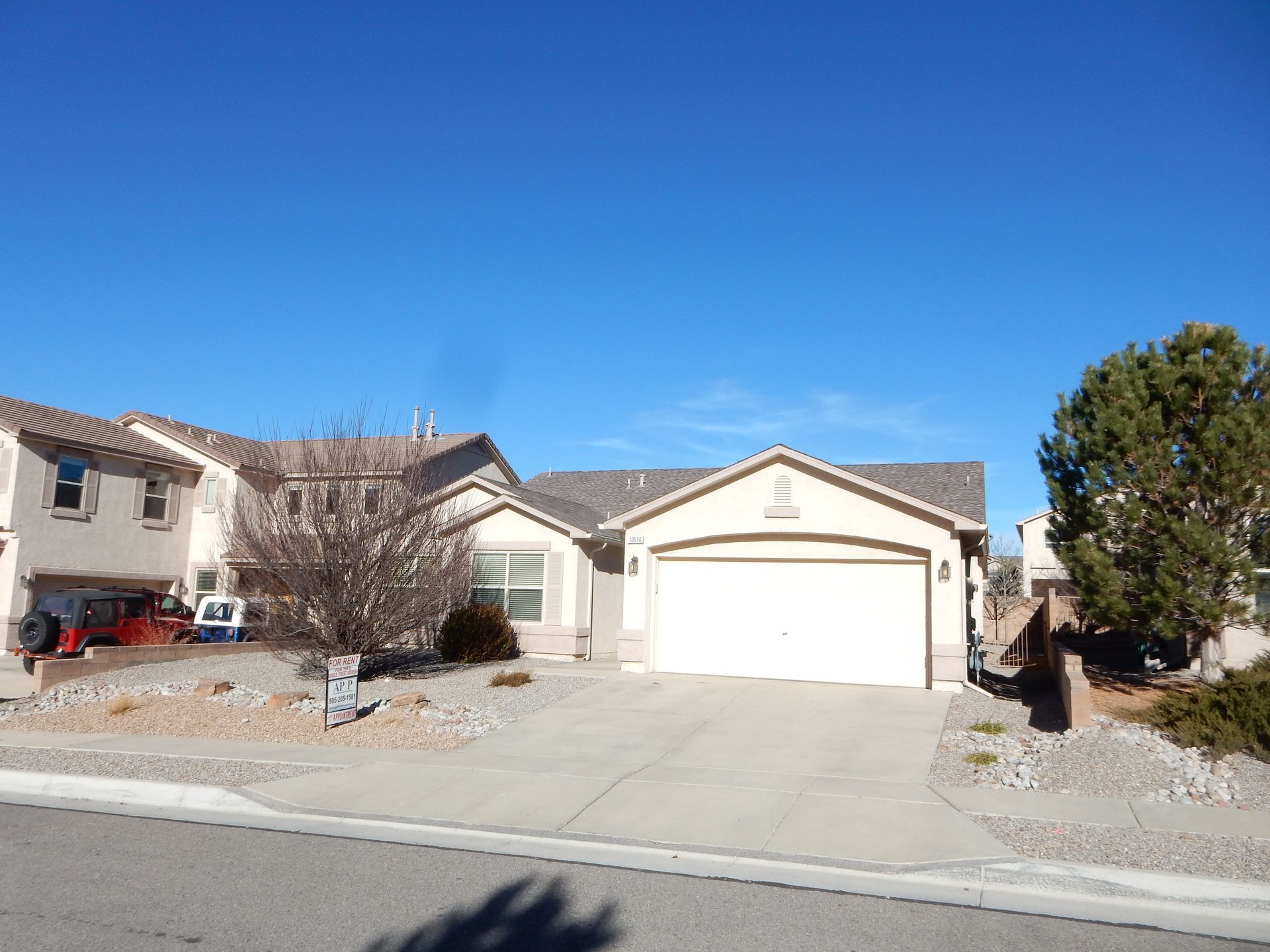 House with a two-car garage, driveway, and rock landscaping under a clear blue sky.