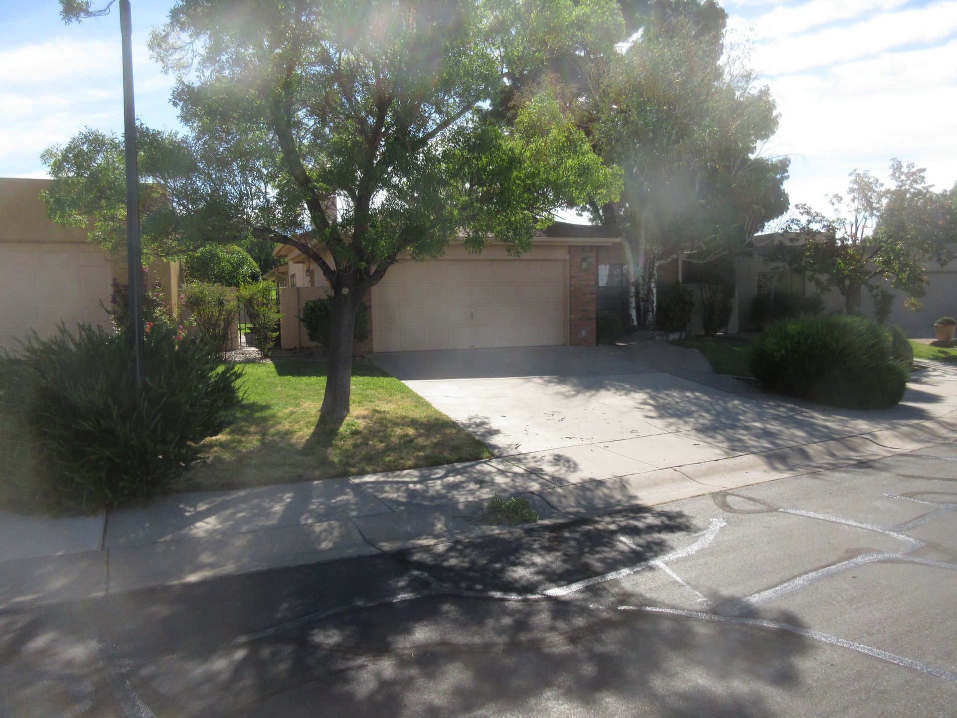 A house with a garage and driveway, with trees and shrubs in front. The sky is visible.