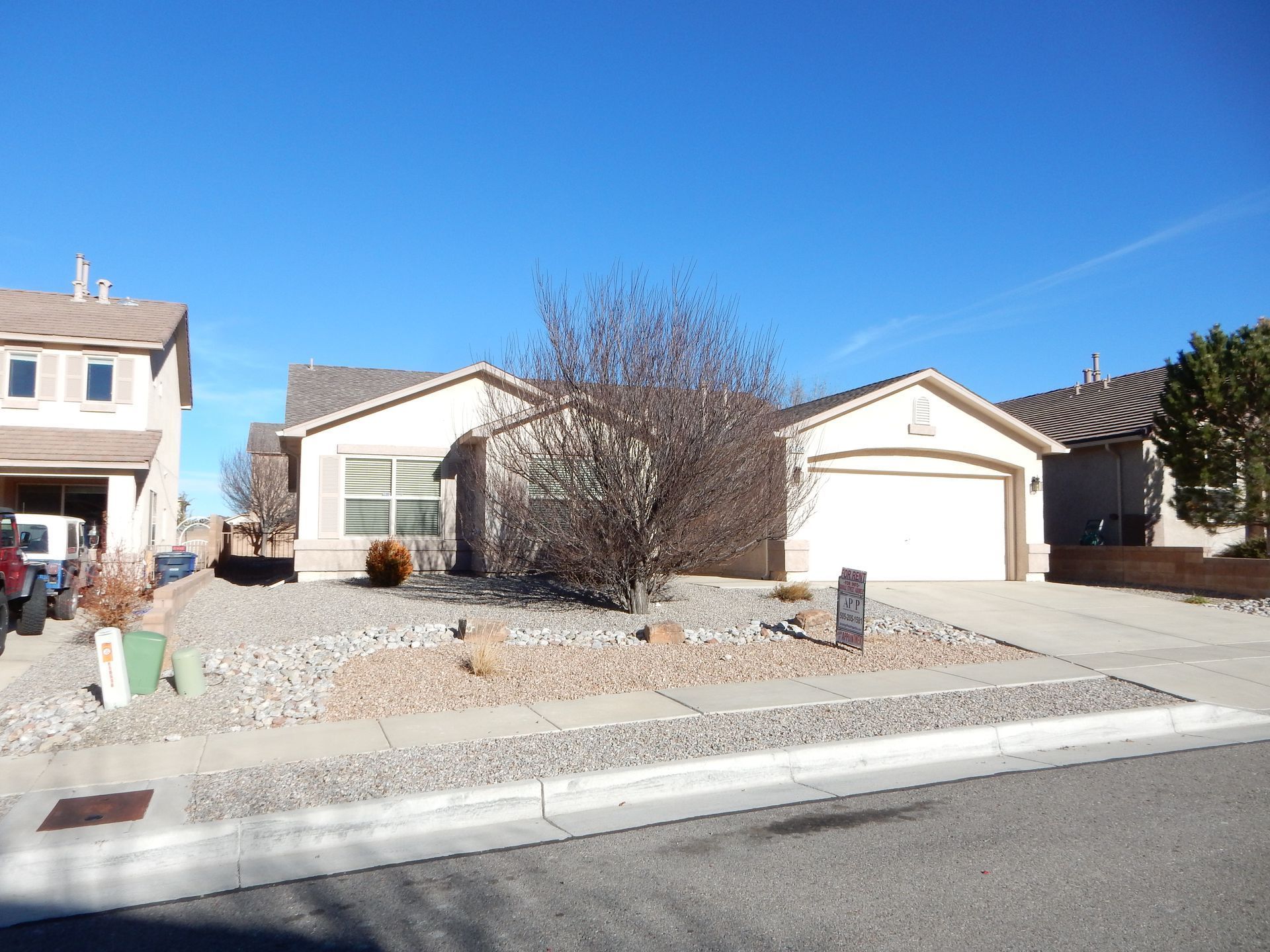 Beige suburban house with gravel landscaping, clear blue sky.