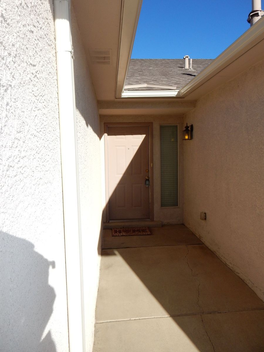 Exterior view of a home's entryway. Light-colored walls, a door, a sidelight, and a concrete path. Sunny.