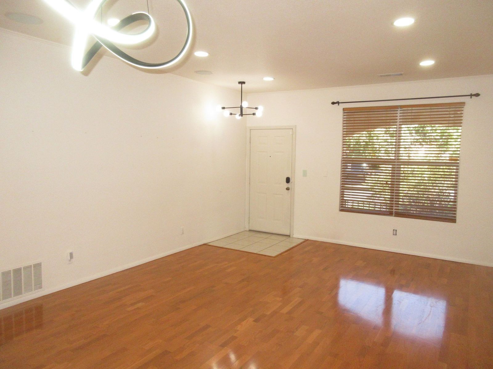 Empty room with hardwood floors, white walls, and a window with a bamboo blind.