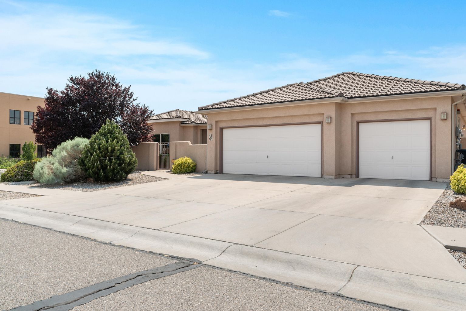 Beige house with two-car garage, driveway, and landscaping on a sunny day.
