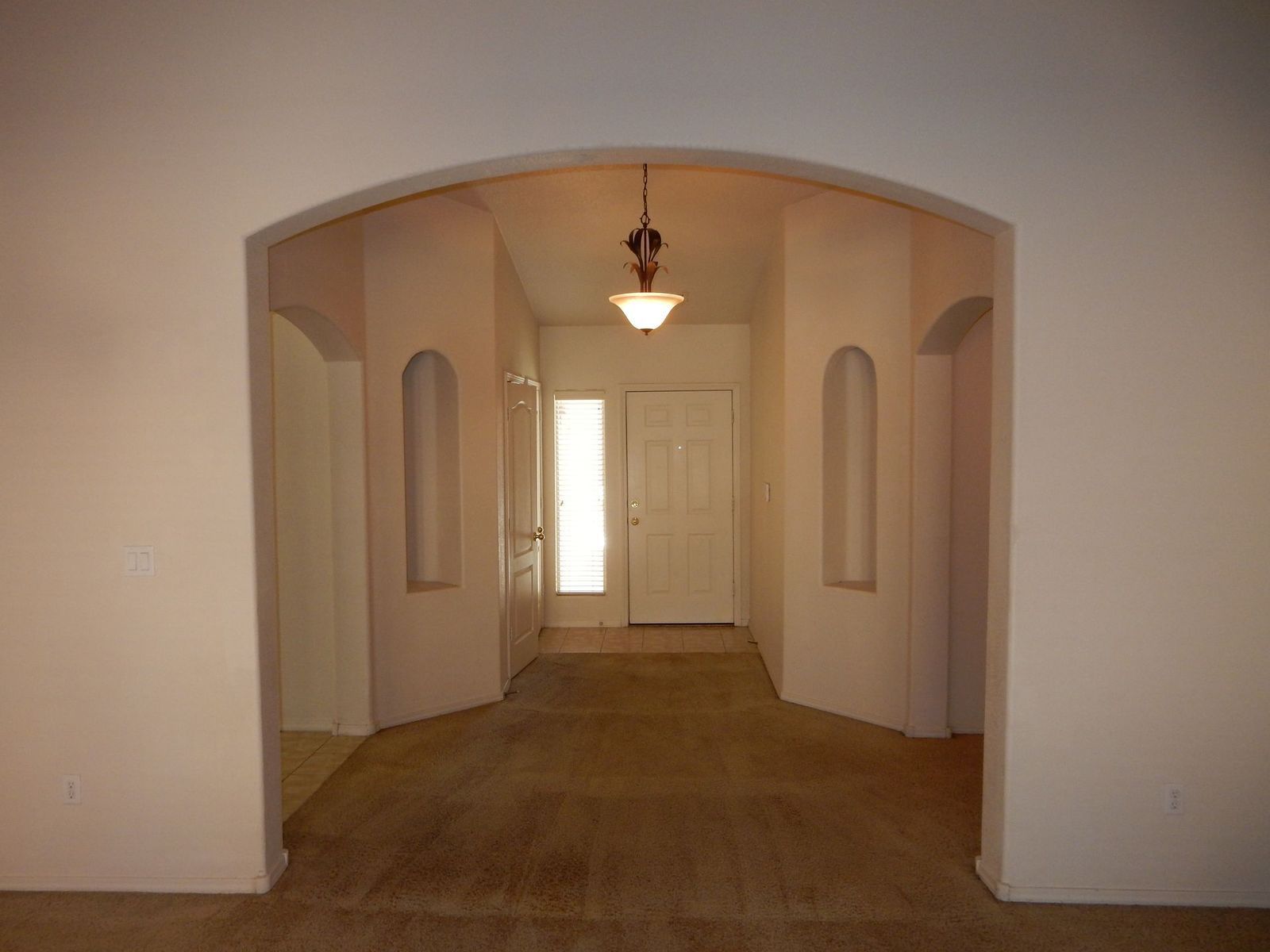 Interior doorway arch leading to front door; beige walls, carpet, and trim. Recessed niches flank the doorway.