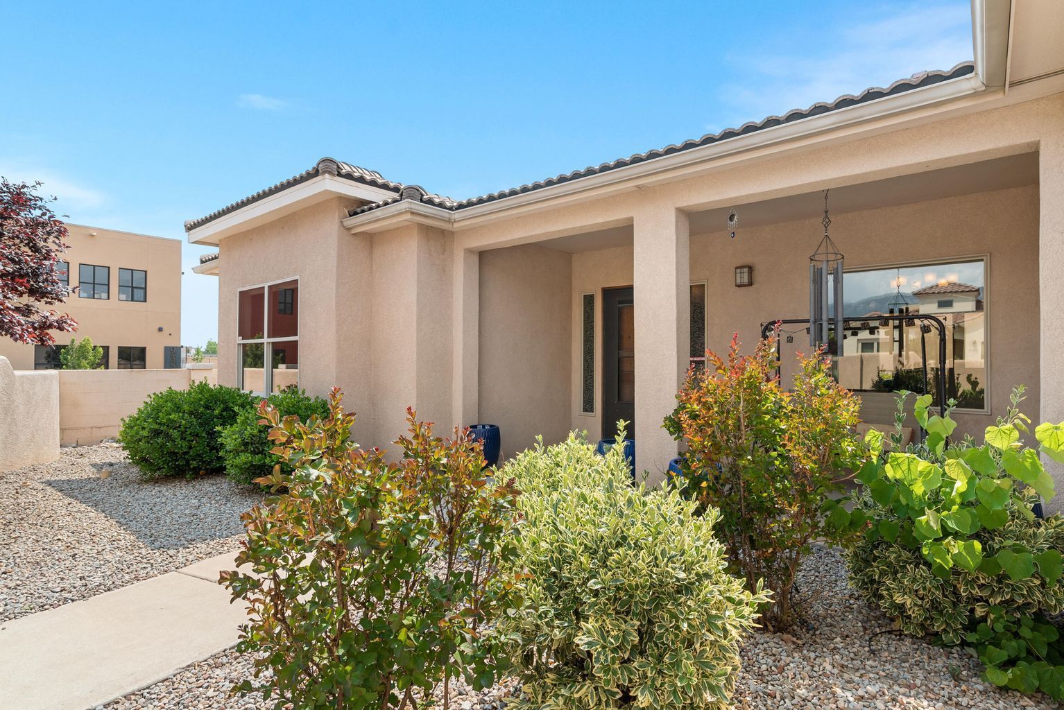 Beige house with porch, shrubs, gravel path, and blue sky.