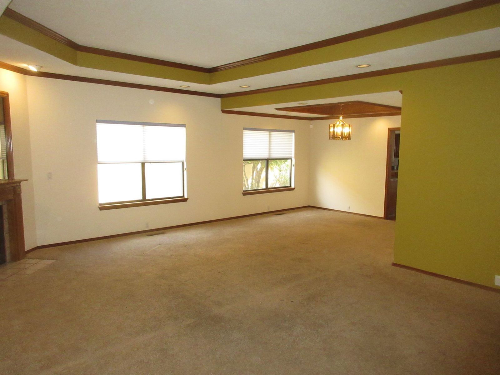 Empty living room with tan carpet, cream walls, and brown trim.
