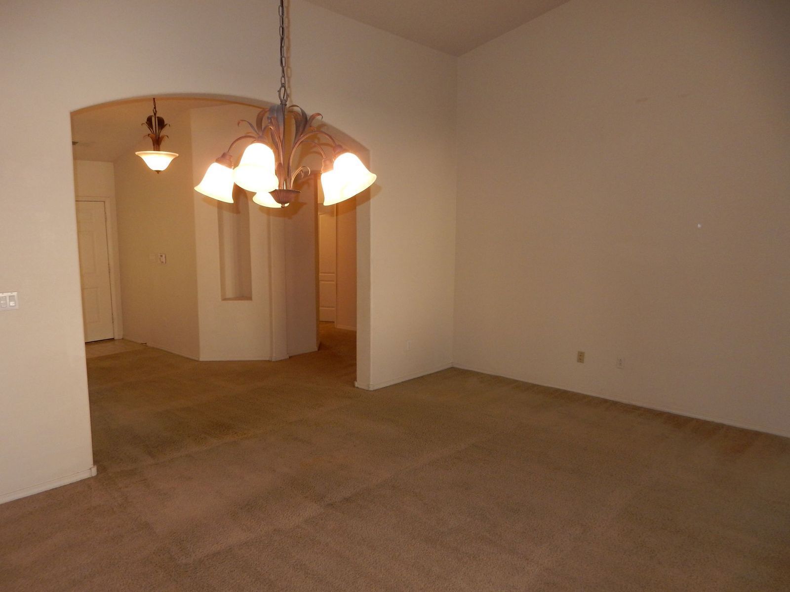 Empty dining room with carpet, chandelier, and archway leading to other rooms.