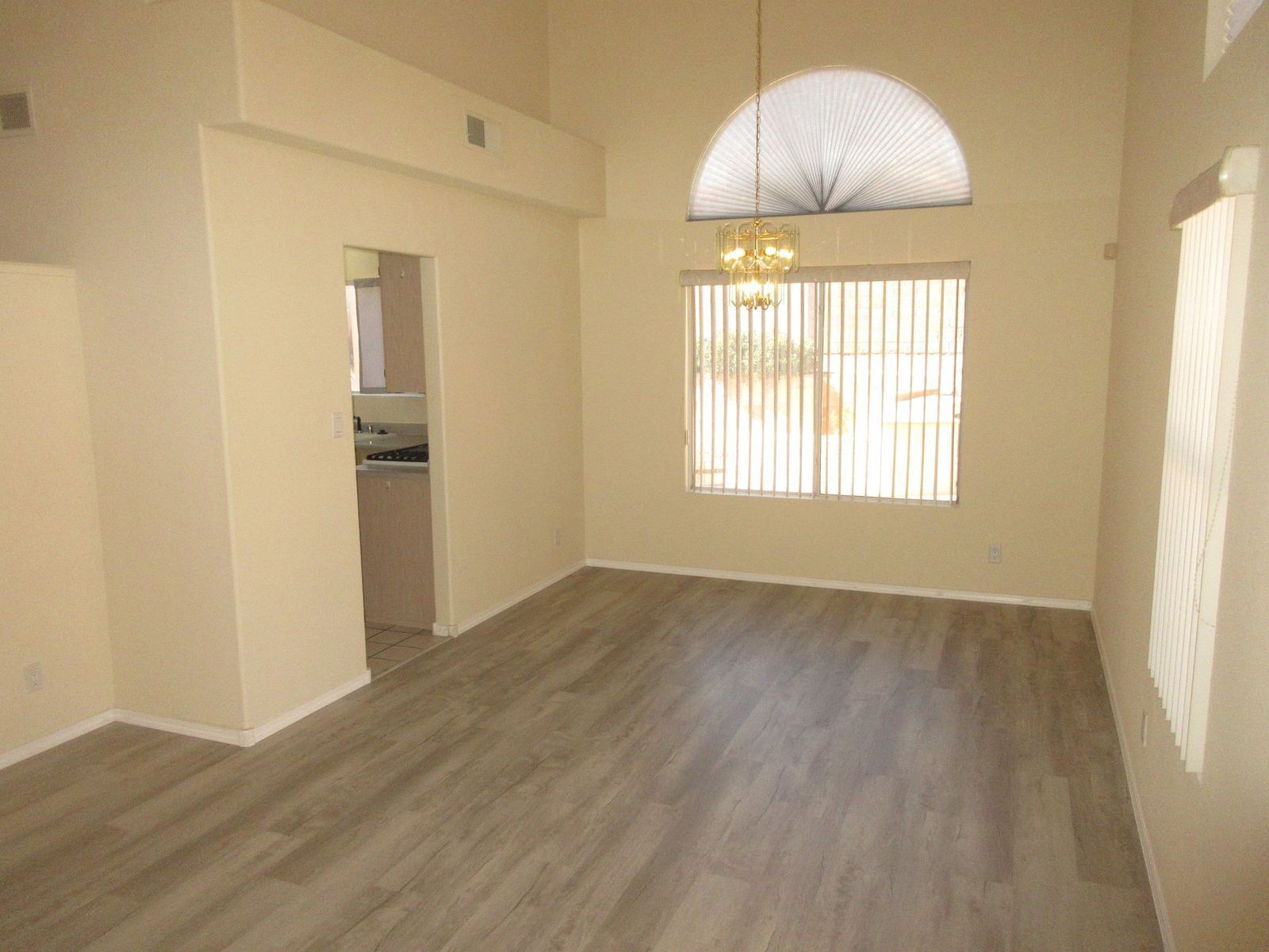 Empty dining room with wood-look floor, large window, and arched ceiling detail; adjacent to kitchen doorway.
