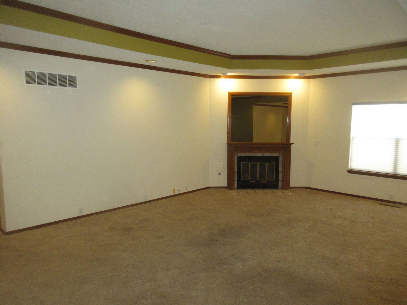 Empty living room with fireplace, beige carpet, and decorative ceiling trim.