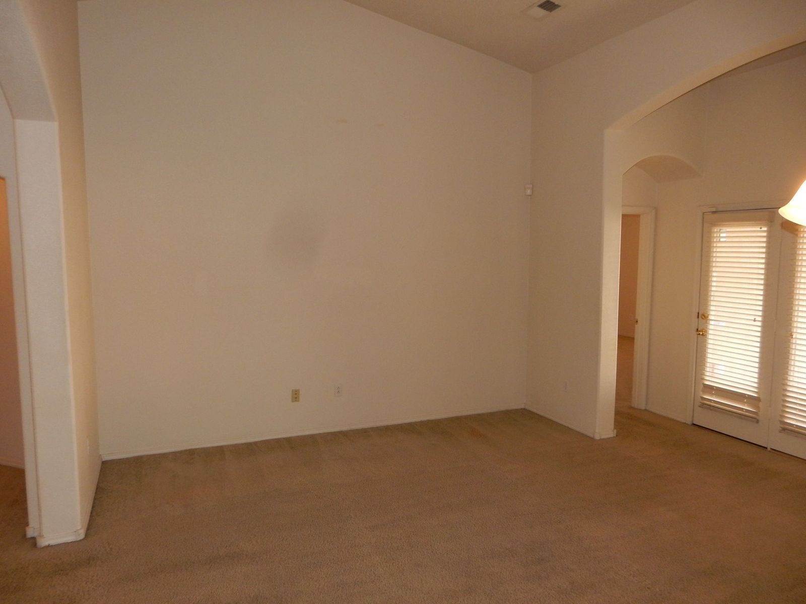 Empty room with beige carpet and light walls, archway to another room.