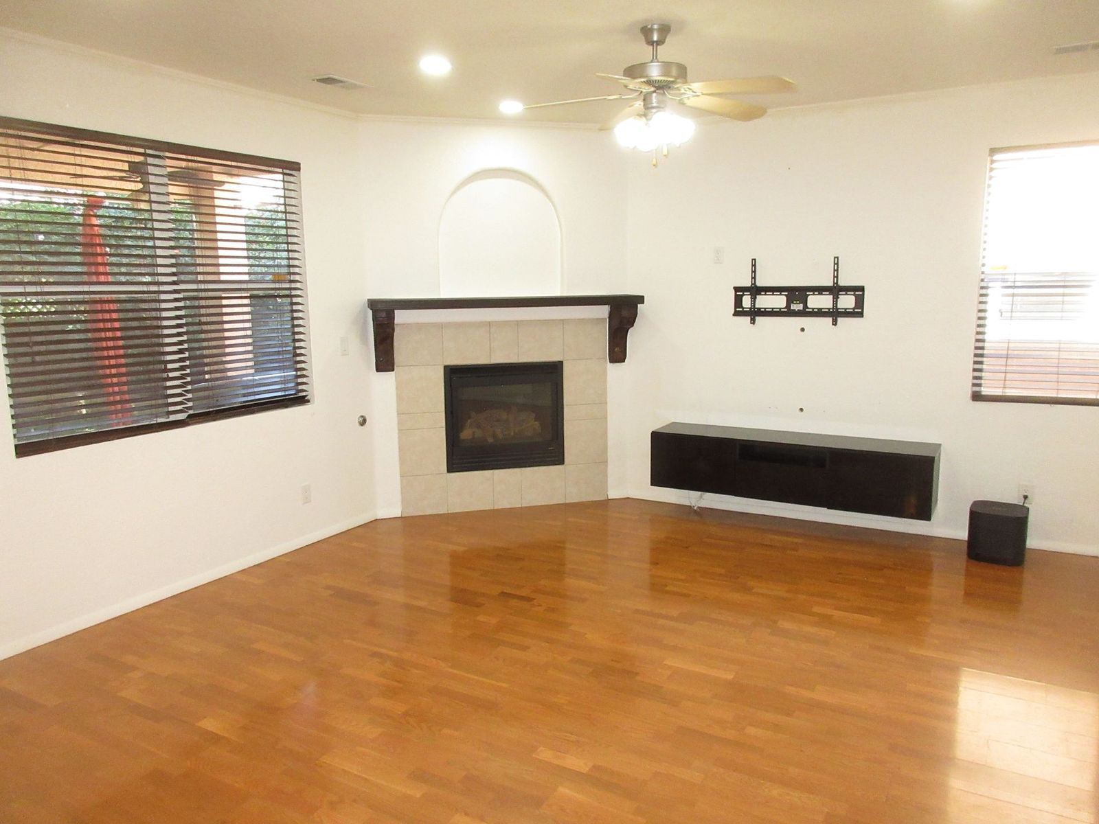 Empty living room with fireplace, built-in entertainment center, and wood floors.