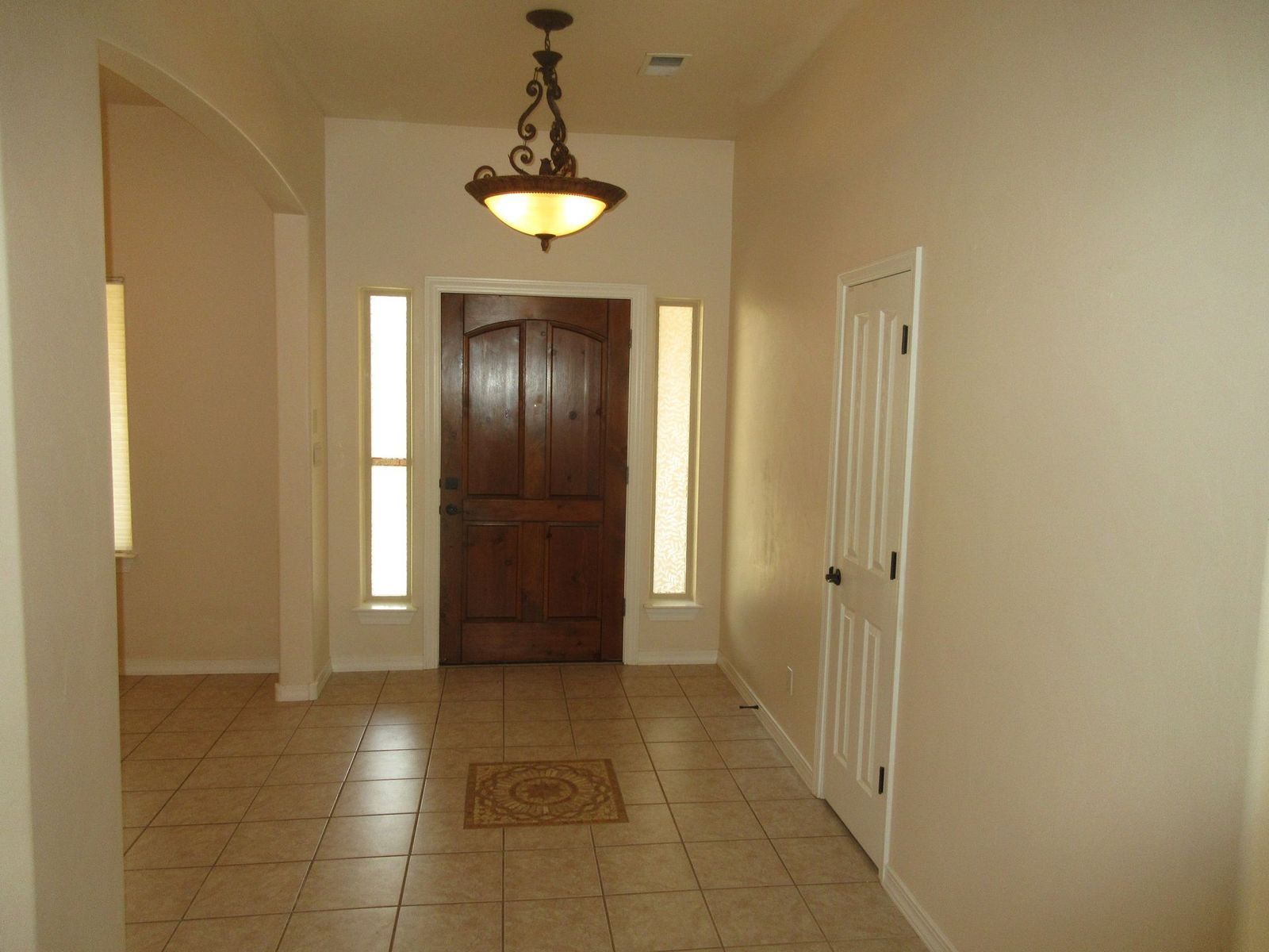 Entryway with brown wooden door, sidelights, cream-colored walls, tile floor, and a decorative light fixture.