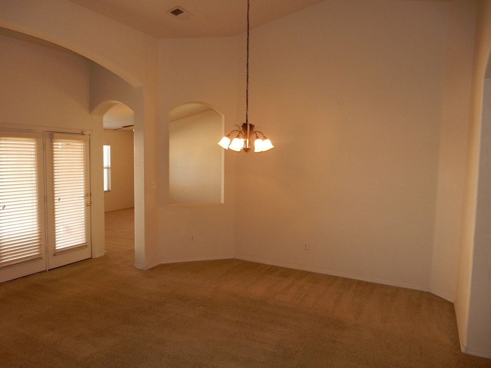 Empty dining room with carpet, chandelier, arched doorways, and a window. Beige walls.