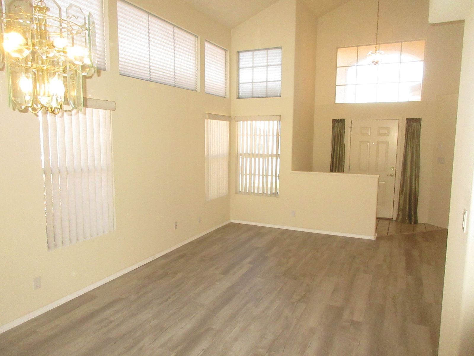 Empty living room with light grey wood-look flooring, tall windows, and a high ceiling.