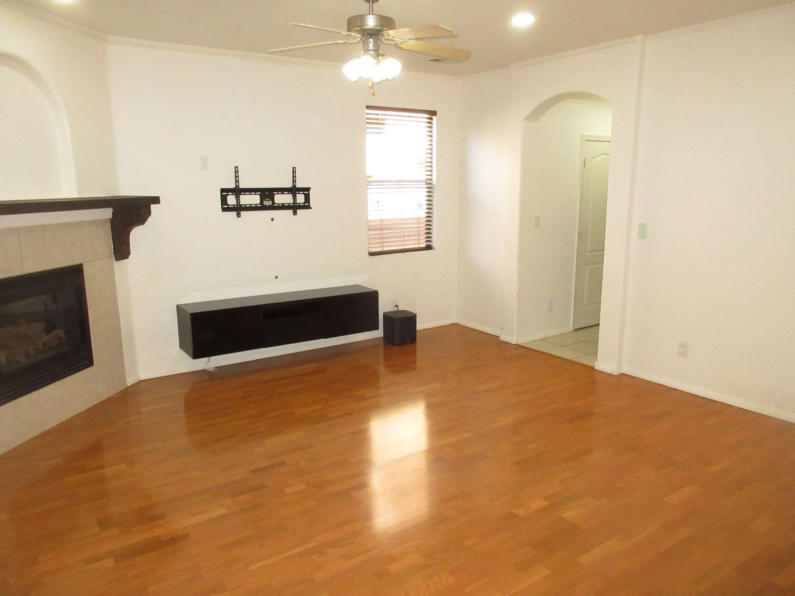 Empty living room with wood floor, fireplace, and mounted TV bracket.
