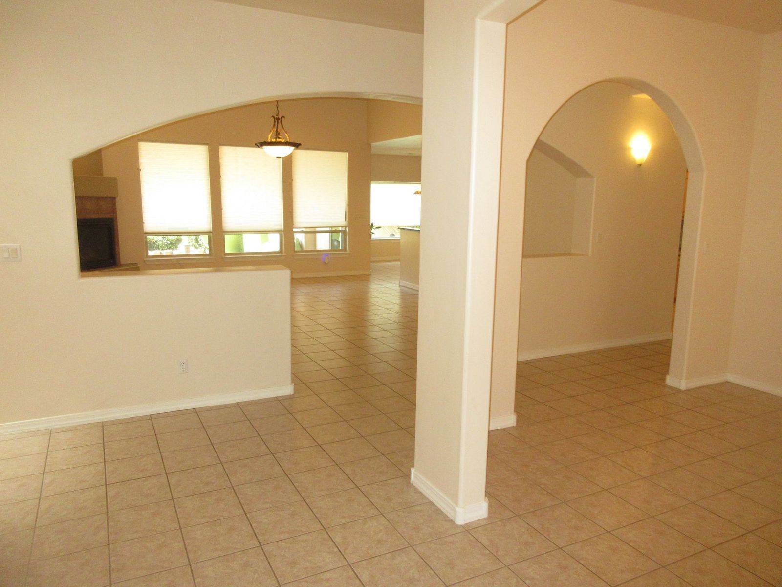 Empty, beige-walled interior with arched doorways, tile floor, and open view to the back, where there are windows.