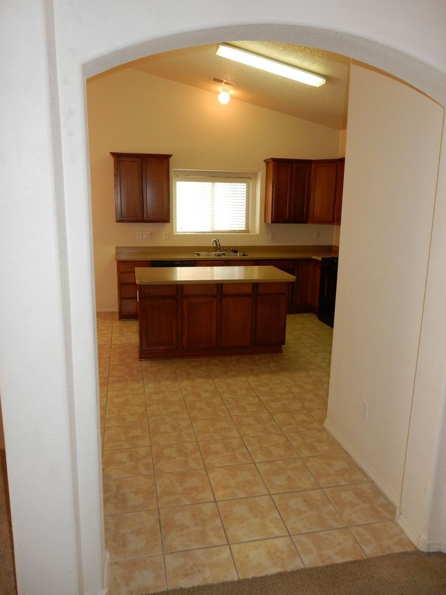 Kitchen with wooden cabinets and island, tile floor, viewed through an arched doorway.