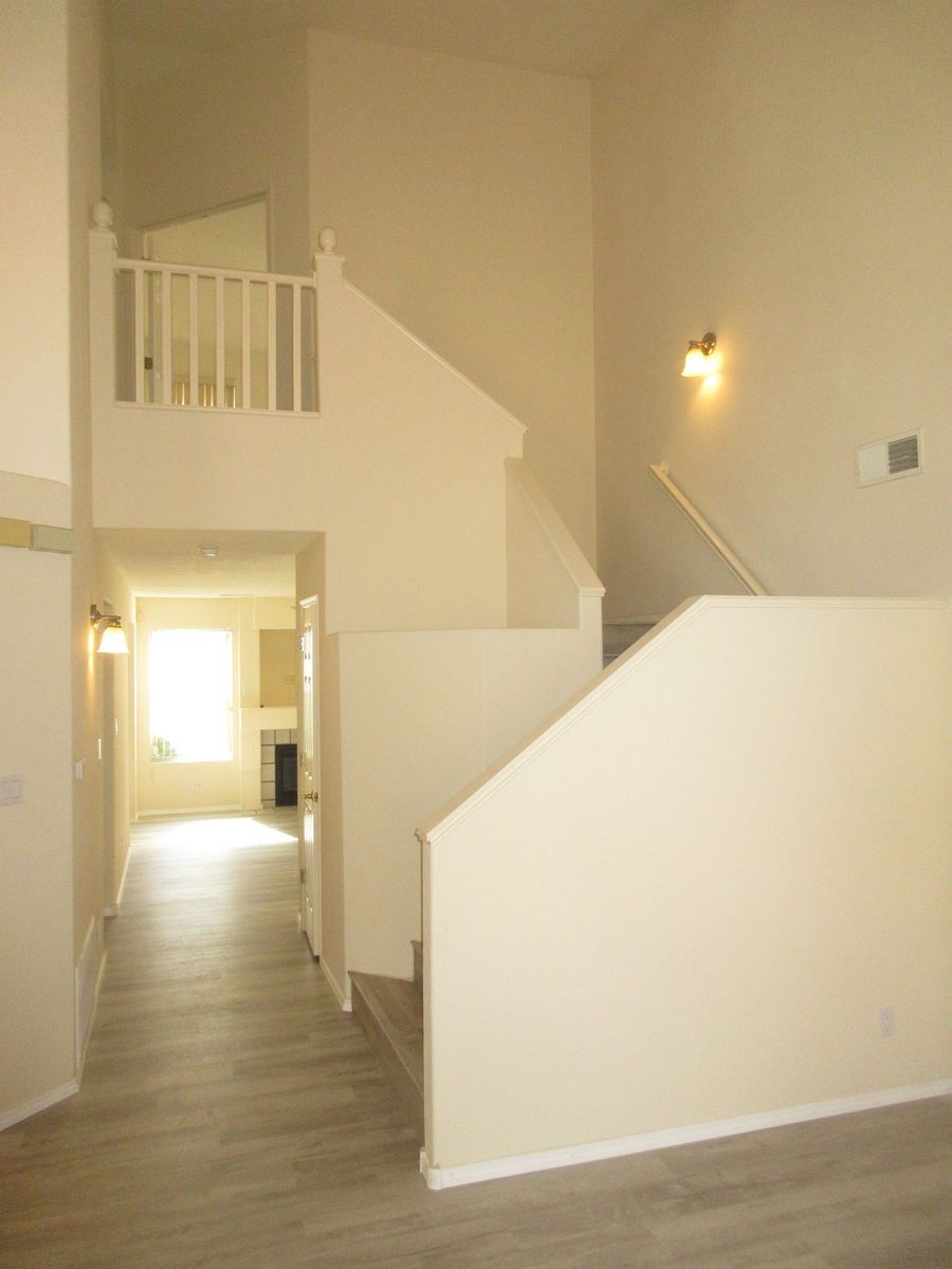Interior view of a two-story home with a staircase, entryway, and a balcony. Neutral-toned walls and flooring.
