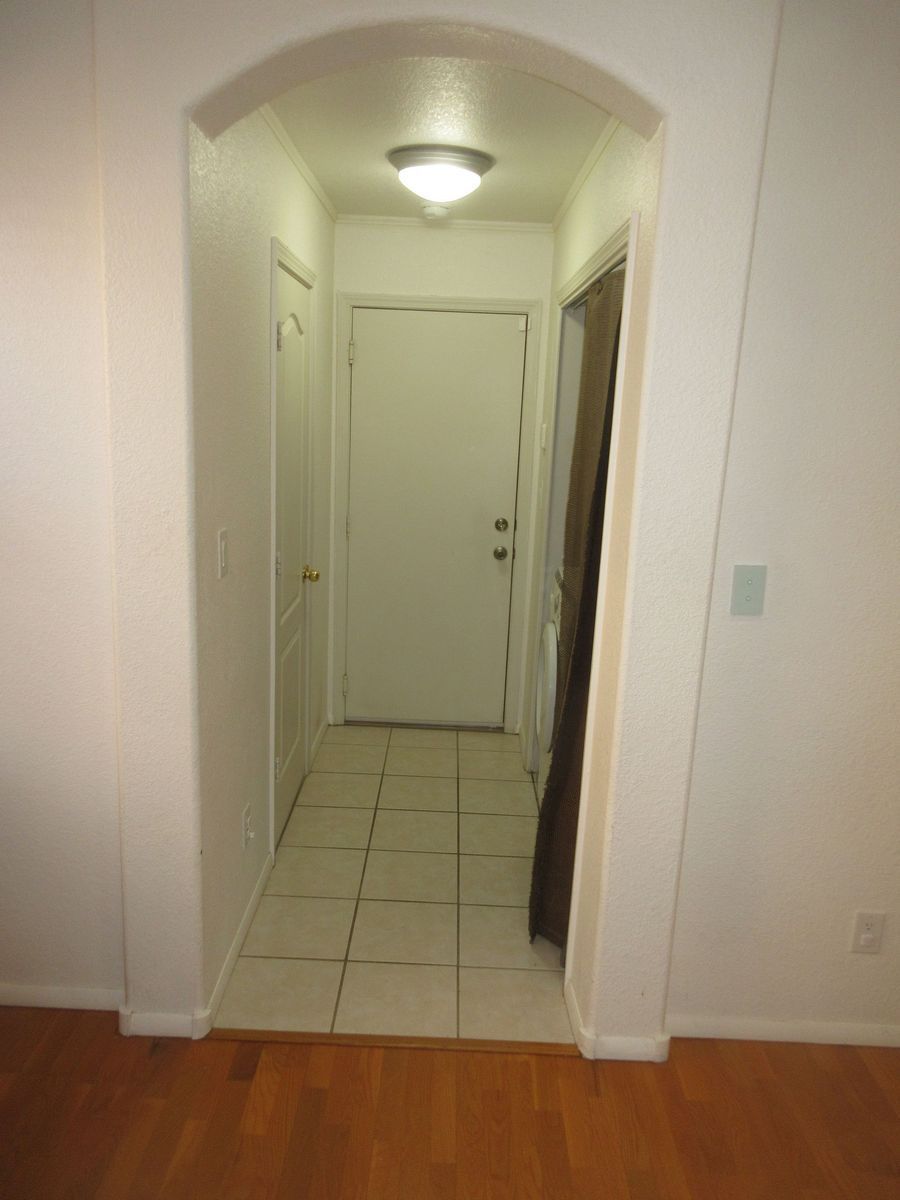 Hallway with arched entryway. White walls, beige tile floor, and a white door at the end.