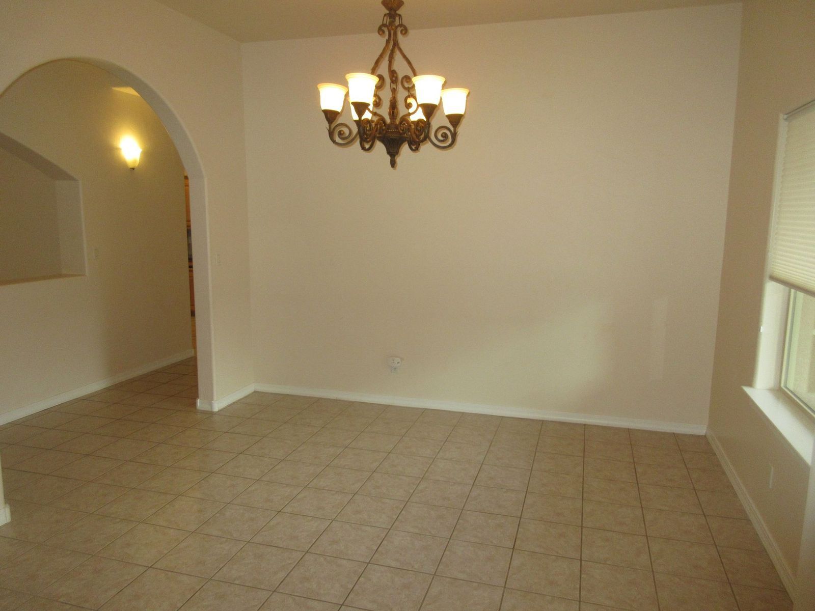 Empty dining room with chandelier, arched doorway, and tiled floor.