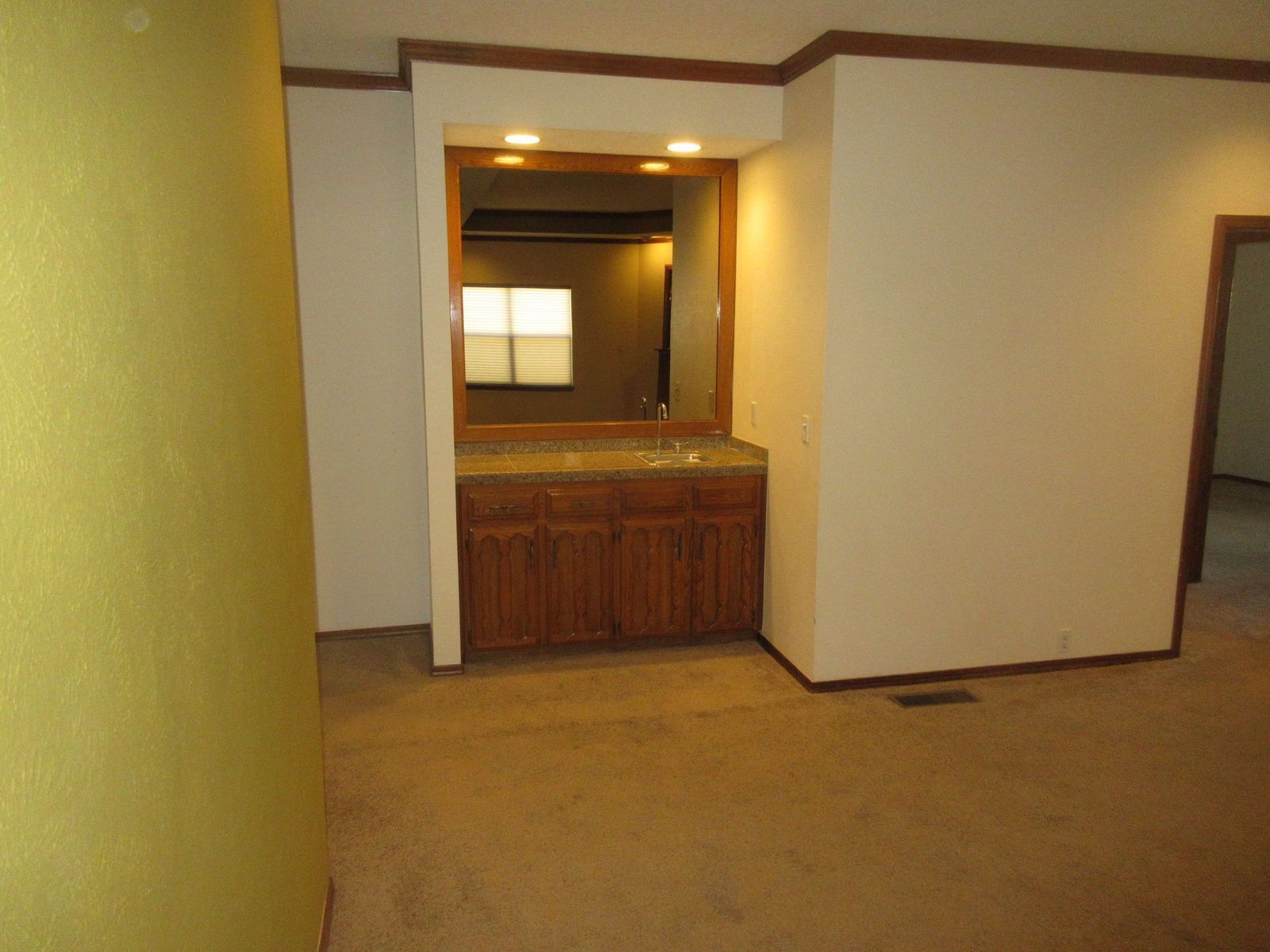 A built-in wet bar with a mirror, cabinets, and a countertop in a room with carpet and beige walls.