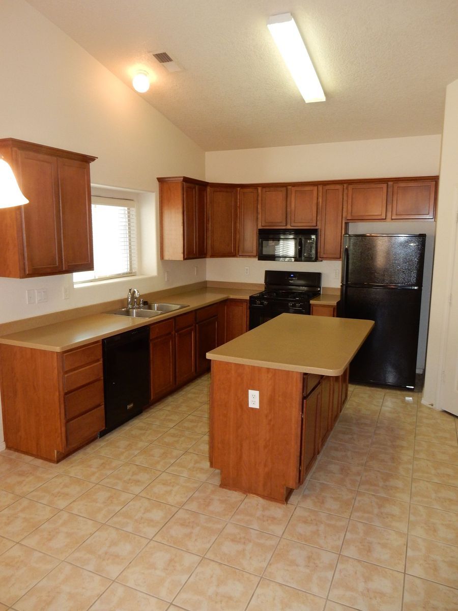 Kitchen with wood cabinets, black appliances, tan countertops, and tiled floor.
