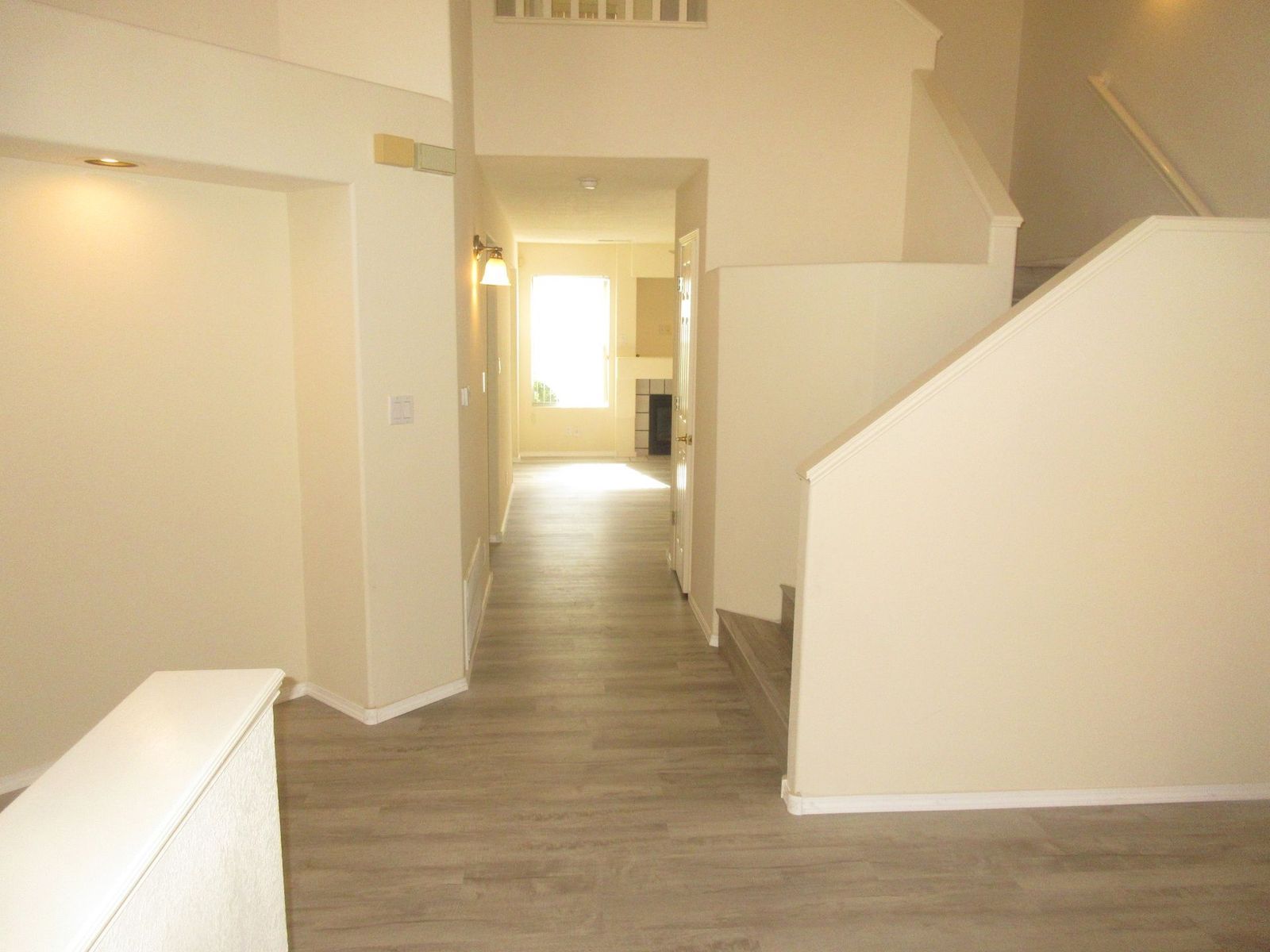 Hallway with staircase, leading to a window. Beige walls and flooring.