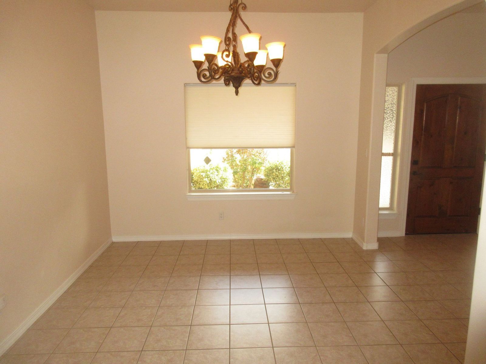 Empty dining room with beige tile floor, window with a shade, chandelier.