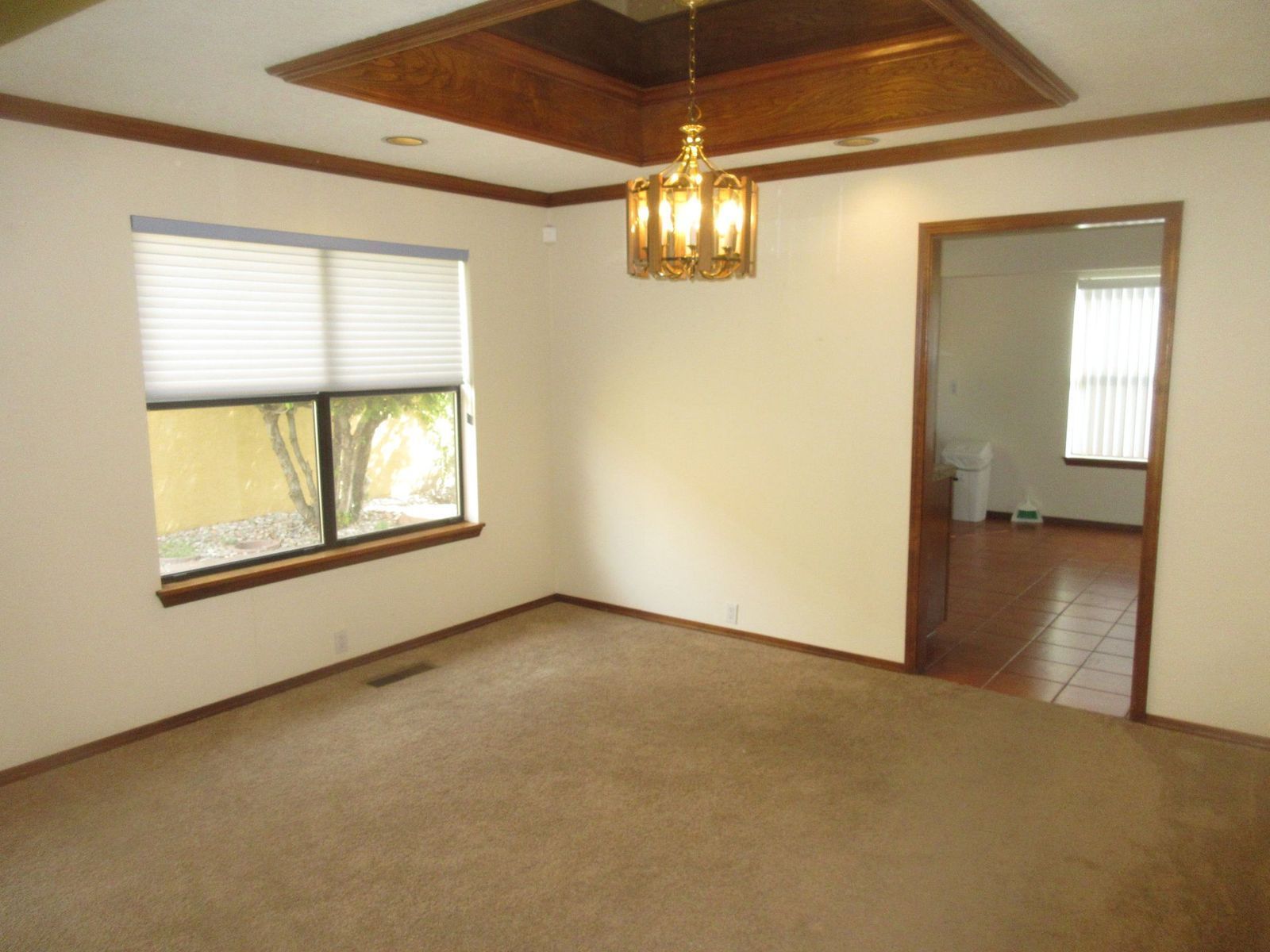 Empty dining room with brown carpet, white walls, and a wood ceiling with a chandelier.