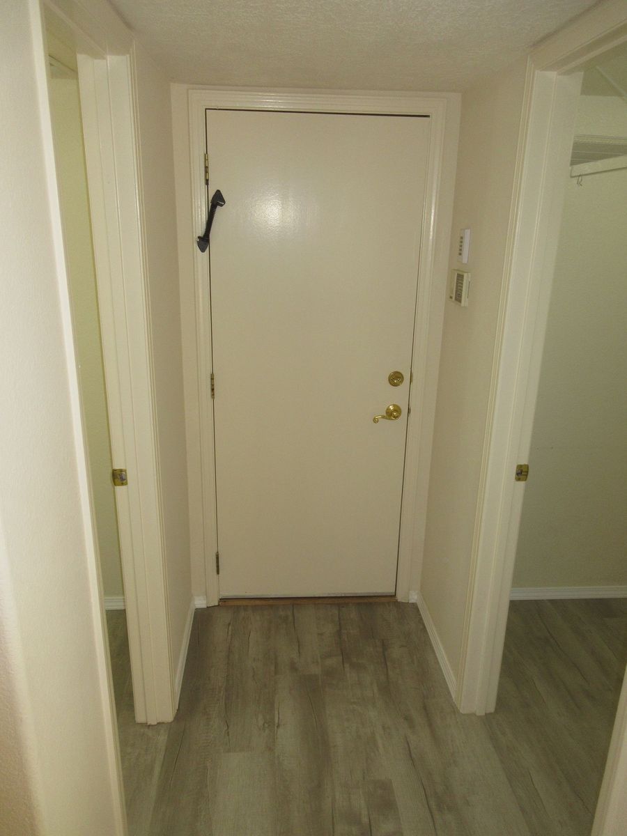Hallway with a door at the end; two doors on either side, all painted white. Gray wood-look flooring.