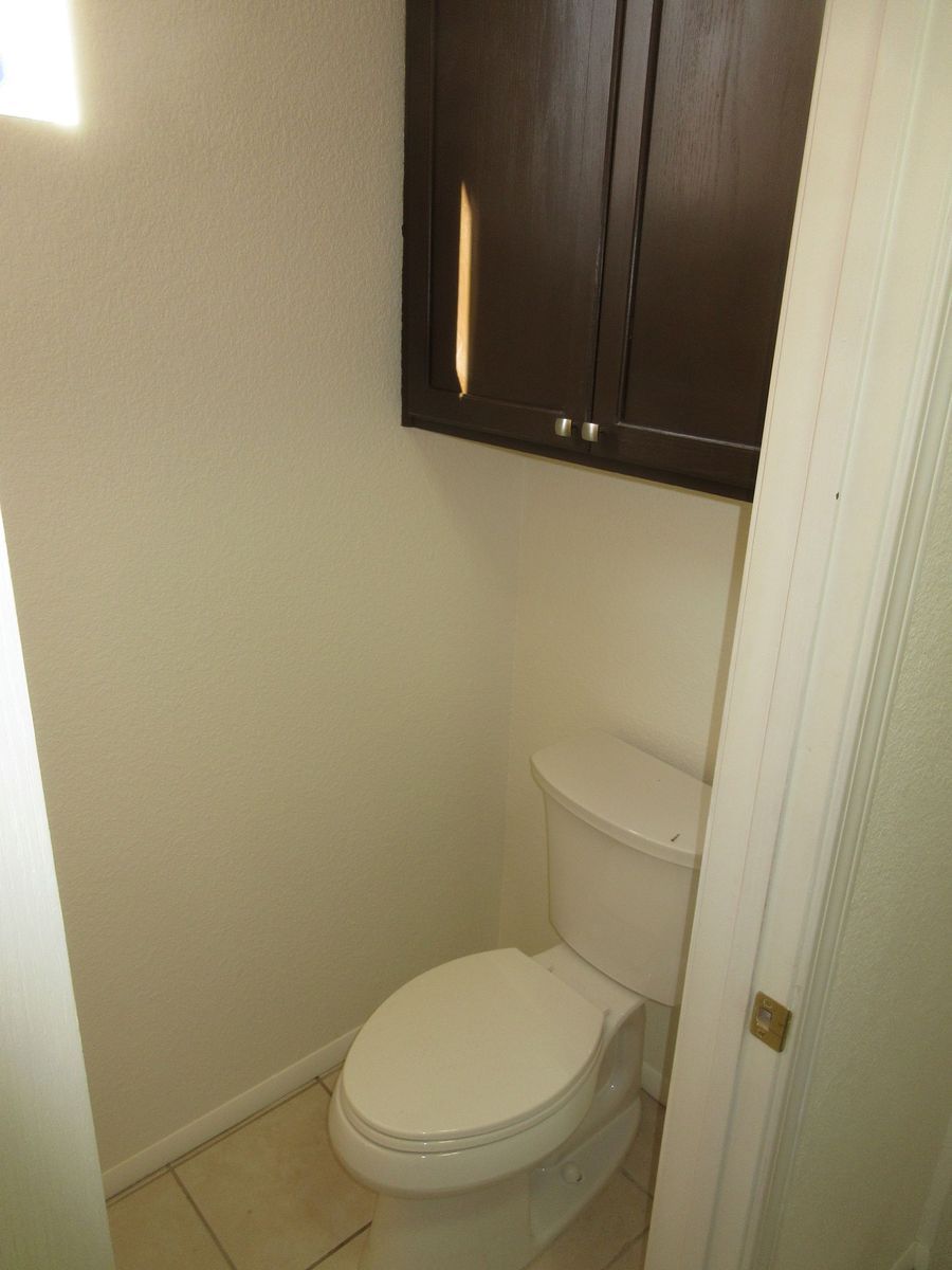 Small bathroom with white toilet, dark brown cabinet, and beige walls.