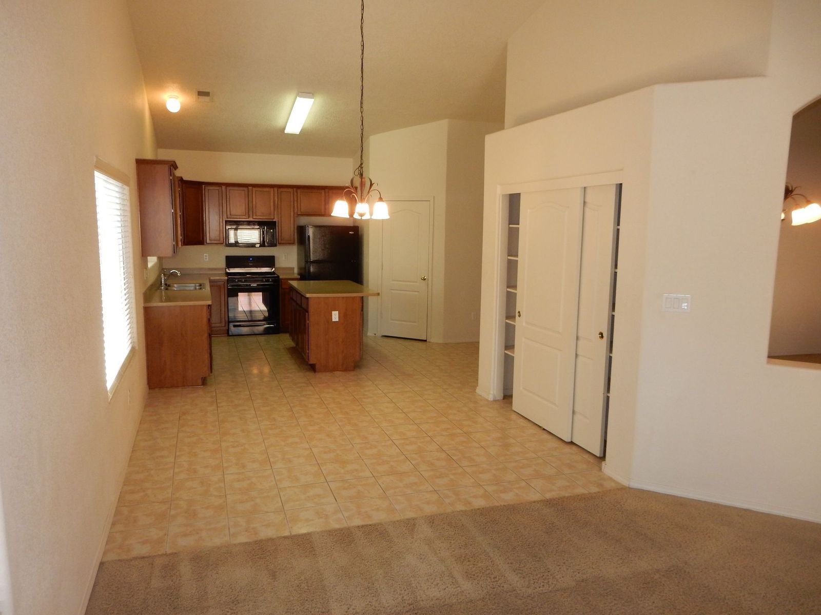 Open-concept kitchen and living area with wood cabinets, tan tile floor, and a closet.