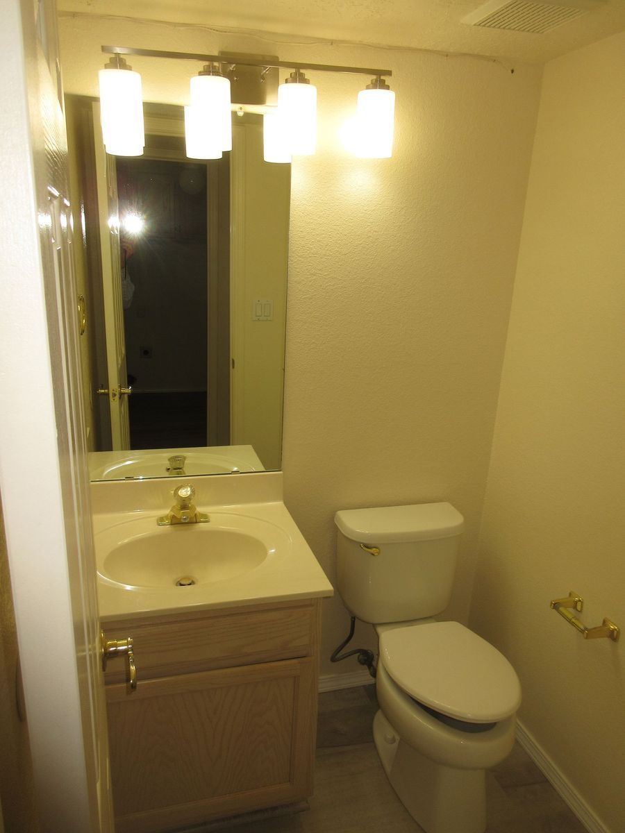 Small bathroom with sink, toilet, mirror, and overhead light fixture. Beige walls, white fixtures.