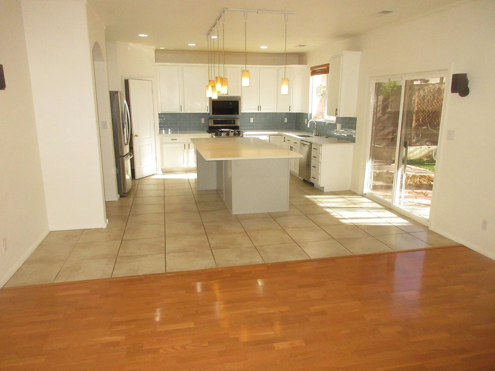 Open-plan kitchen with white cabinets, large island, and light wood floors, leading to a sliding door and backyard.