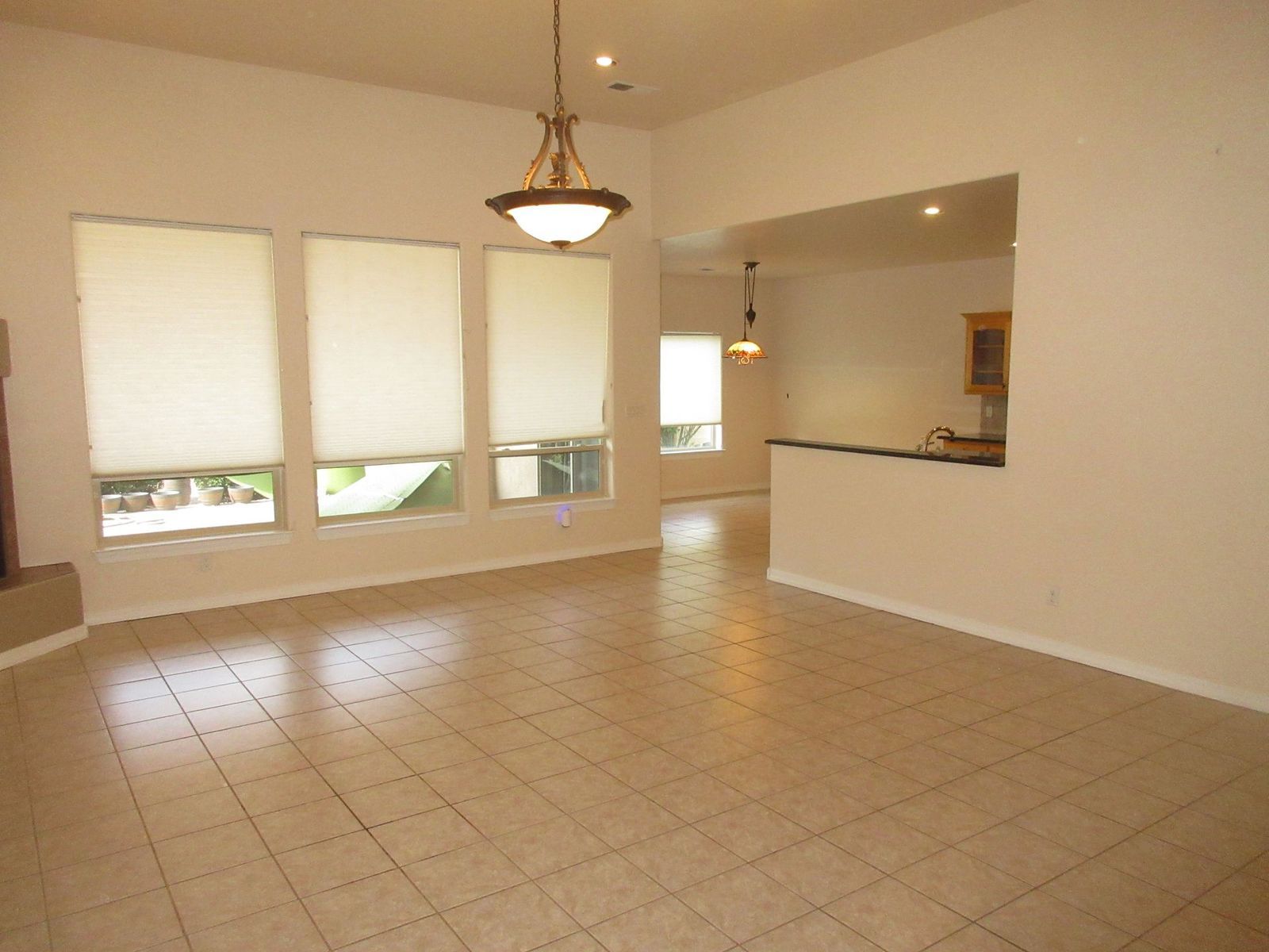 Empty living room with tiled floor, three large windows, and an opening to the kitchen area.