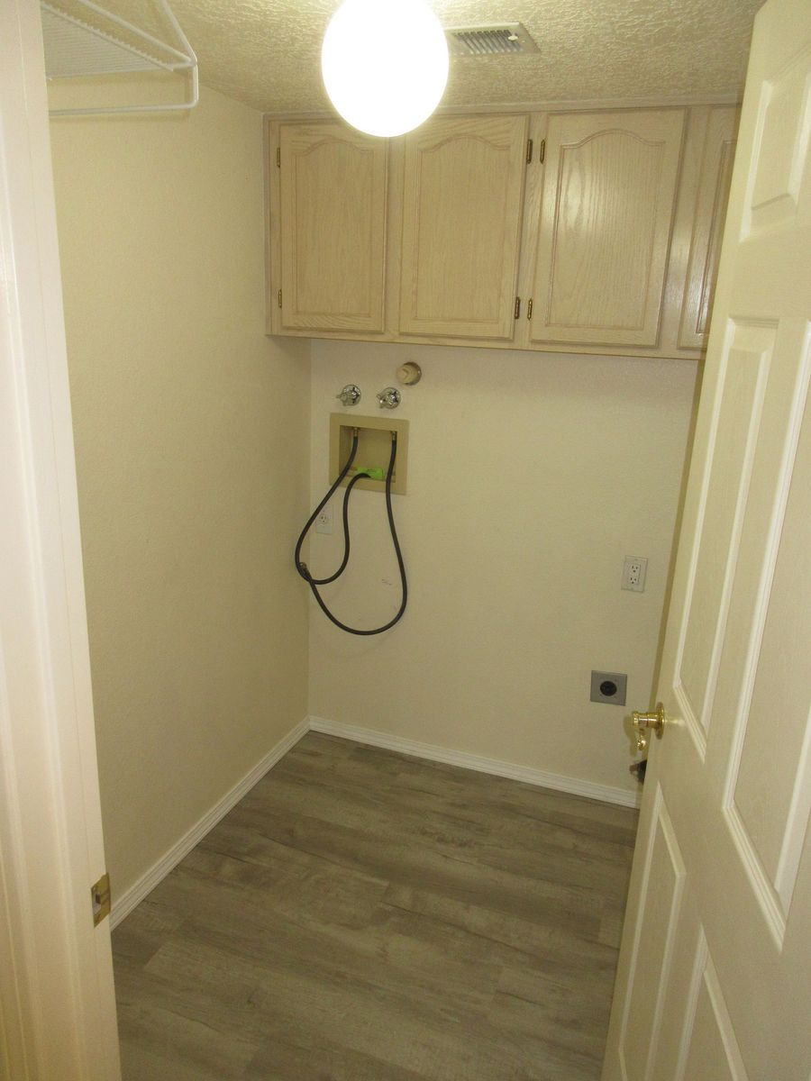 Laundry room with upper cabinets, washing machine connections, and a doorway. Light-colored walls and flooring.