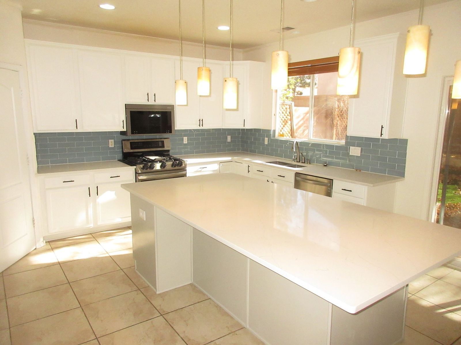 Modern white kitchen with a large island, blue backsplash, and pendant lights.