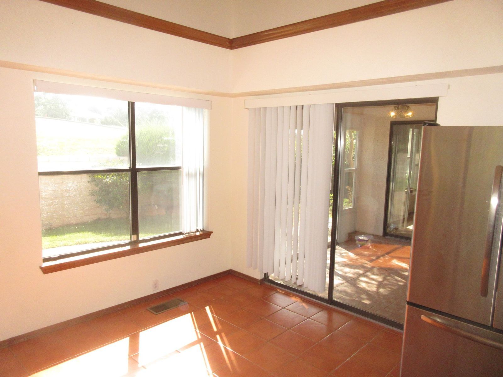 Corner kitchen with windows, sliding glass door, brown tile floor, and stainless steel refrigerator.
