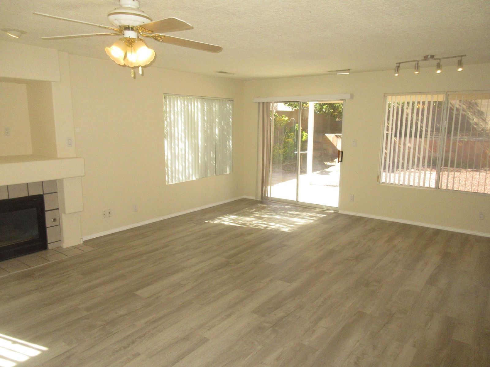 Living room with fireplace, sliding door to patio, wood-look floor, tan walls, and a ceiling fan.