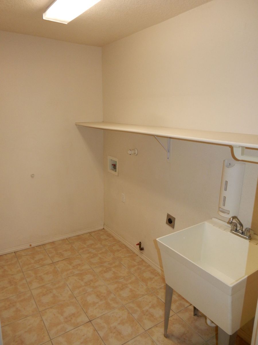 Laundry room with a utility sink, shelf, and tile floor.