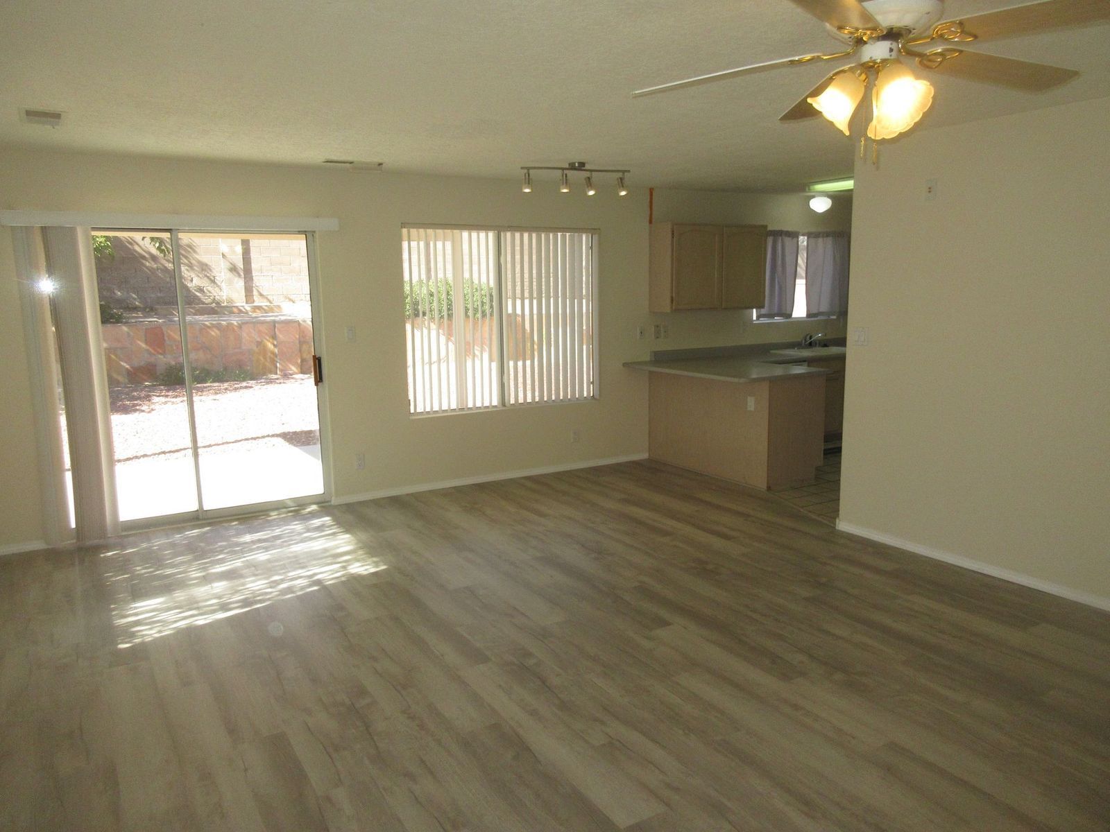 Living room with sliding glass door, kitchen, and light-colored wood-look flooring.