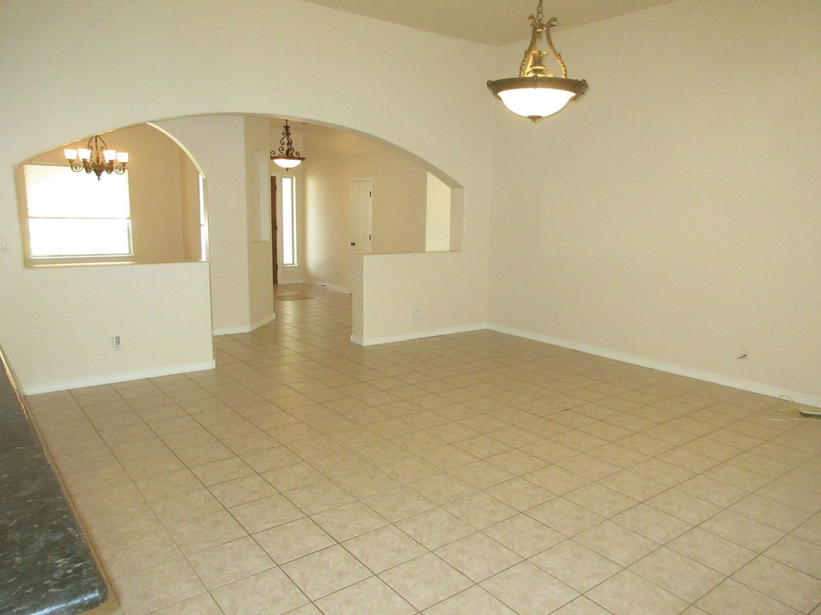 Empty dining and living area with tan tile floors, white walls, and archways.