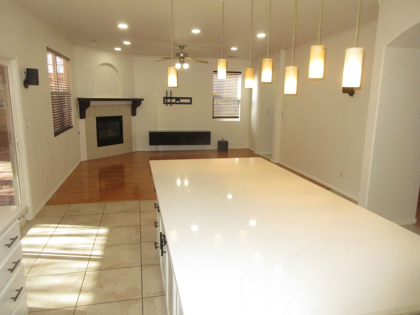 Open-plan kitchen/living area with white countertops, wooden floors, fireplace, and hanging lights.