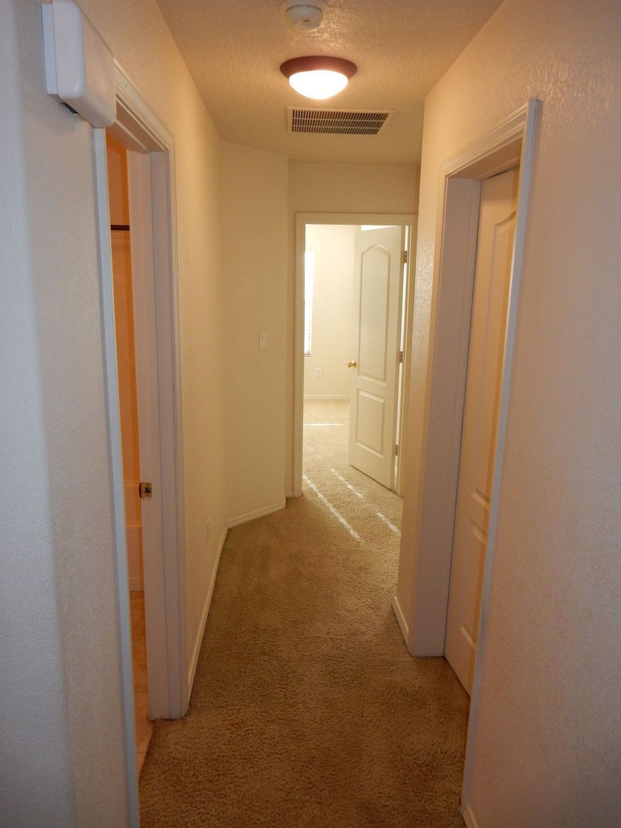 Narrow hallway with carpet, doors on both sides, and a light fixture on the ceiling.