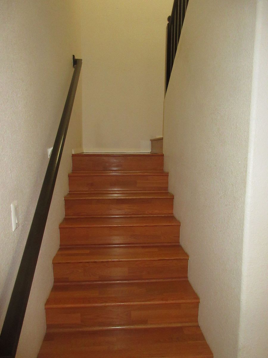 Wooden stairs with dark railing and white walls leading upwards.