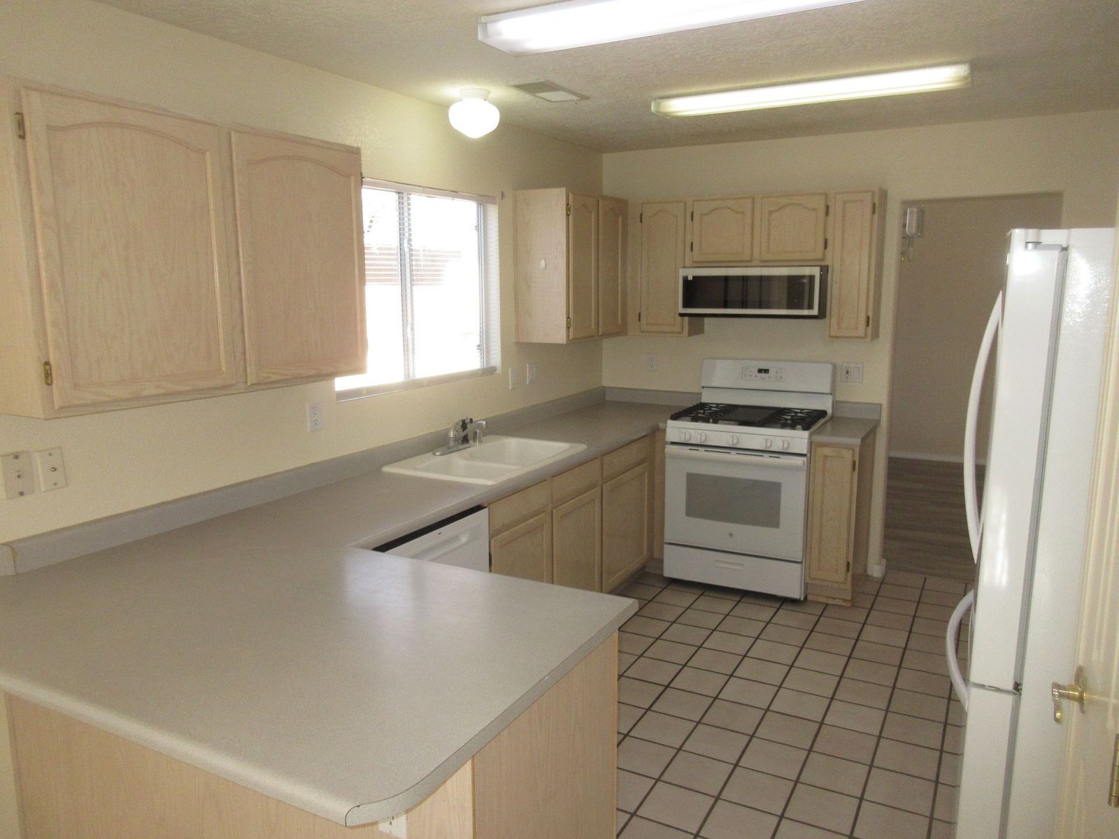 Kitchen with light-colored cabinets, countertops, and appliances, including a stove, microwave, and refrigerator.
