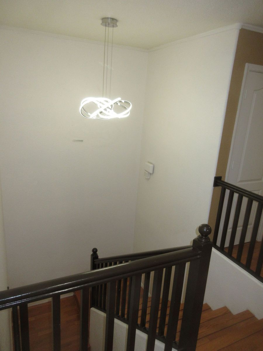 Staircase with wooden railing, leading down. White walls, modern light fixture.