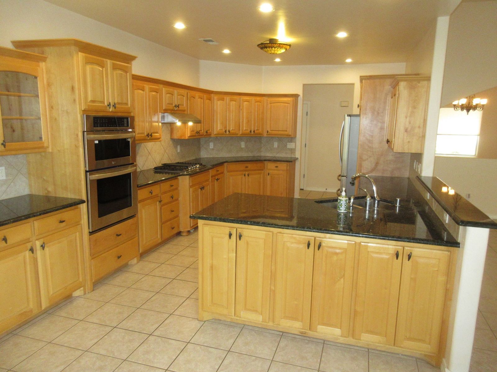 Kitchen with light wood cabinets, black countertops, and a large island.